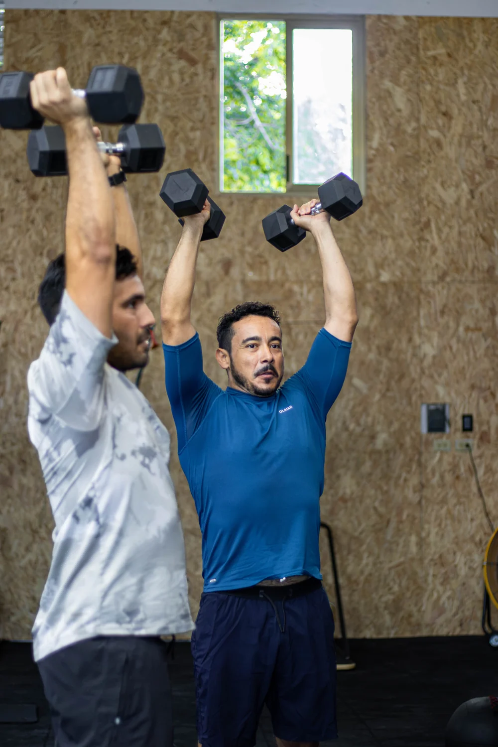 Dos participantes levantando mancuernas por encima de la cabeza