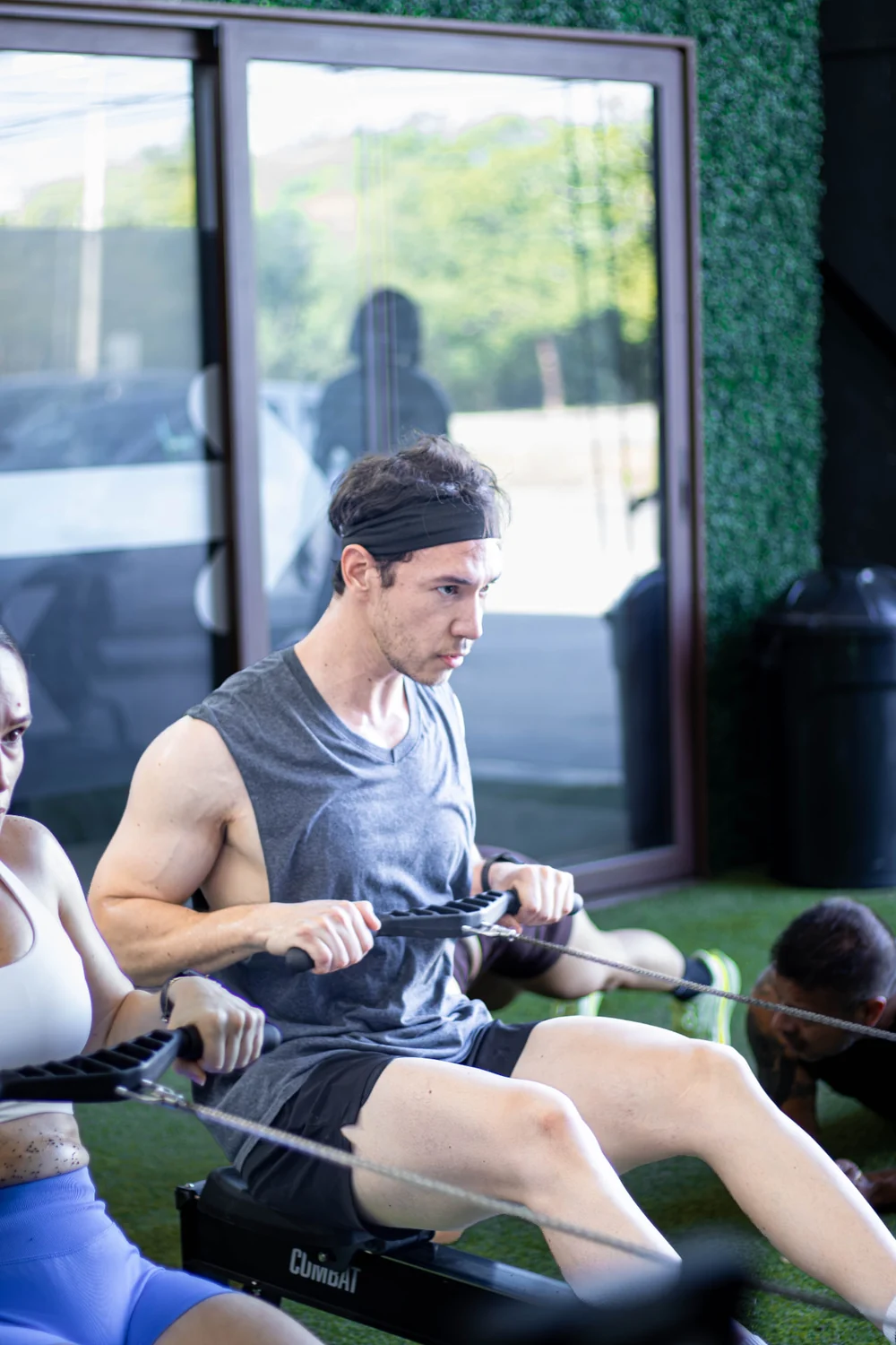 Participantes entrenando en máquinas de remo junto al ventanal del gimnasio
